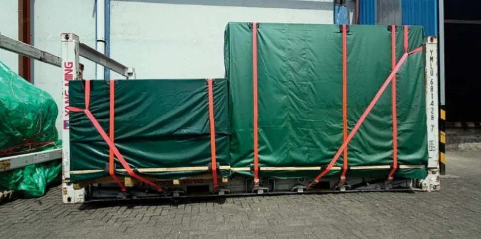 Green tarpaulin-covered loads lashed with orange straps on a flat-rack container