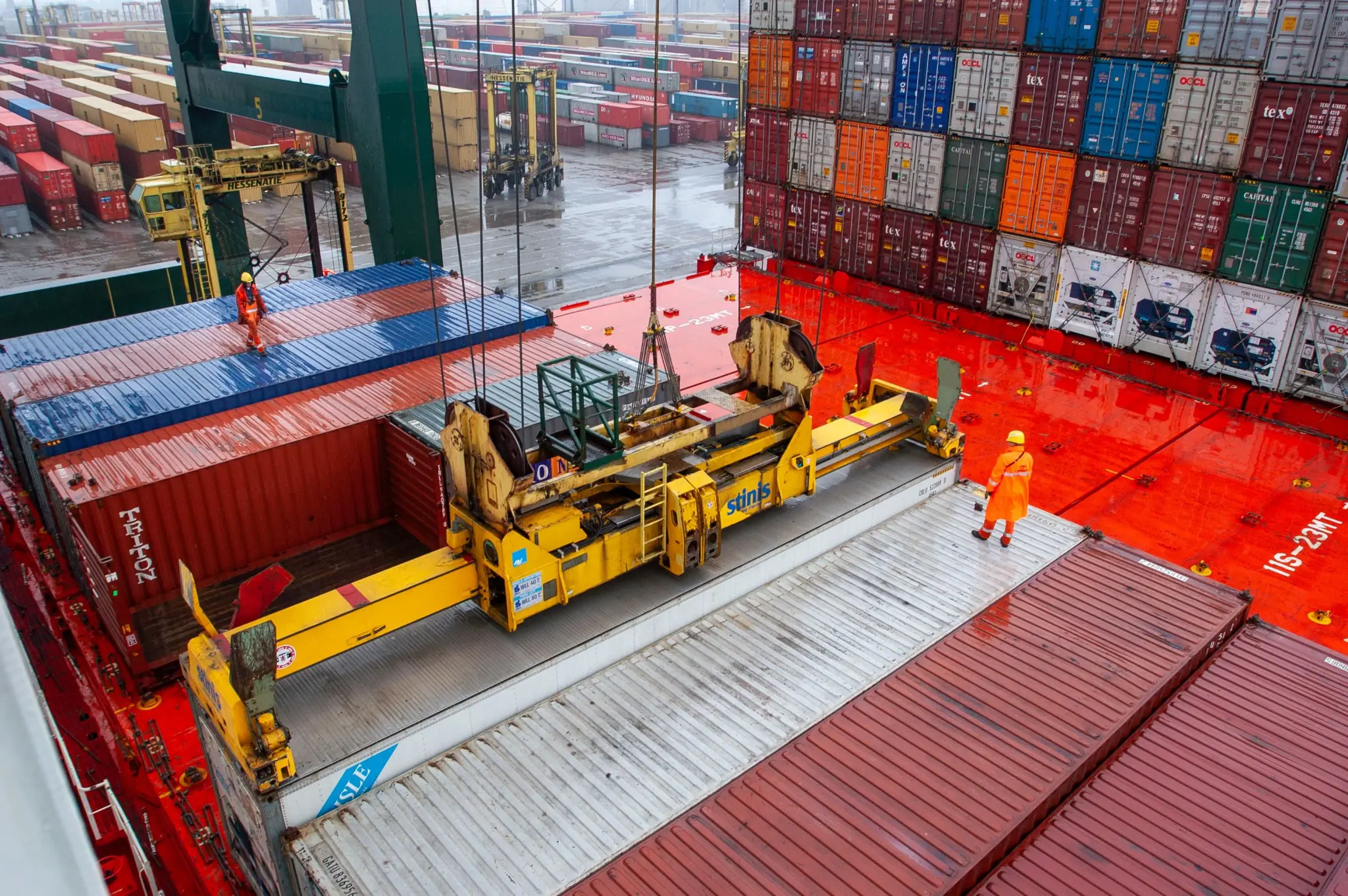 Crane loading containers onto a vessel while workers direct the lift